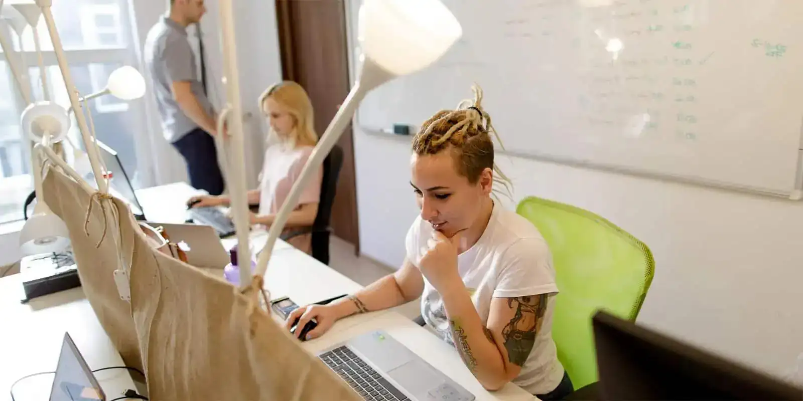 Photo of office room with whiteboard and people working on laptops